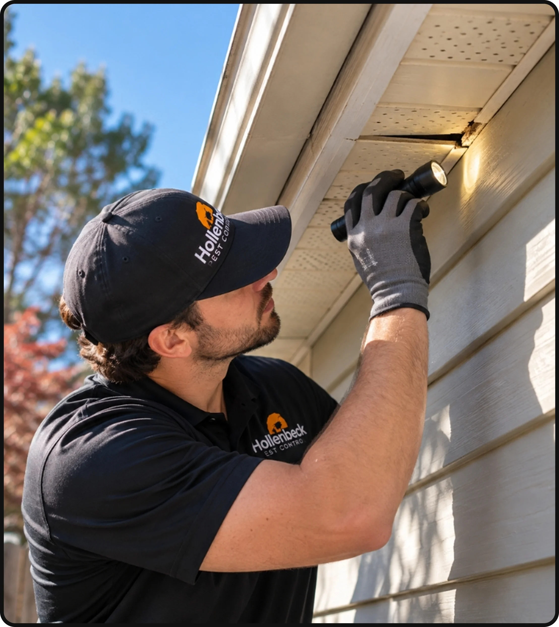 Hollenbeck Pest Control technician inspecting the exterior roofline and soffit of a home for potential pest entry points.